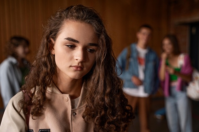 Ein nachdenkliches Mädchen steht im Vordergrund, im Hintergrund eine Gruppe Mitschülerinnen – Symbolbild für Ausgrenzung und Mobbing in der Schule